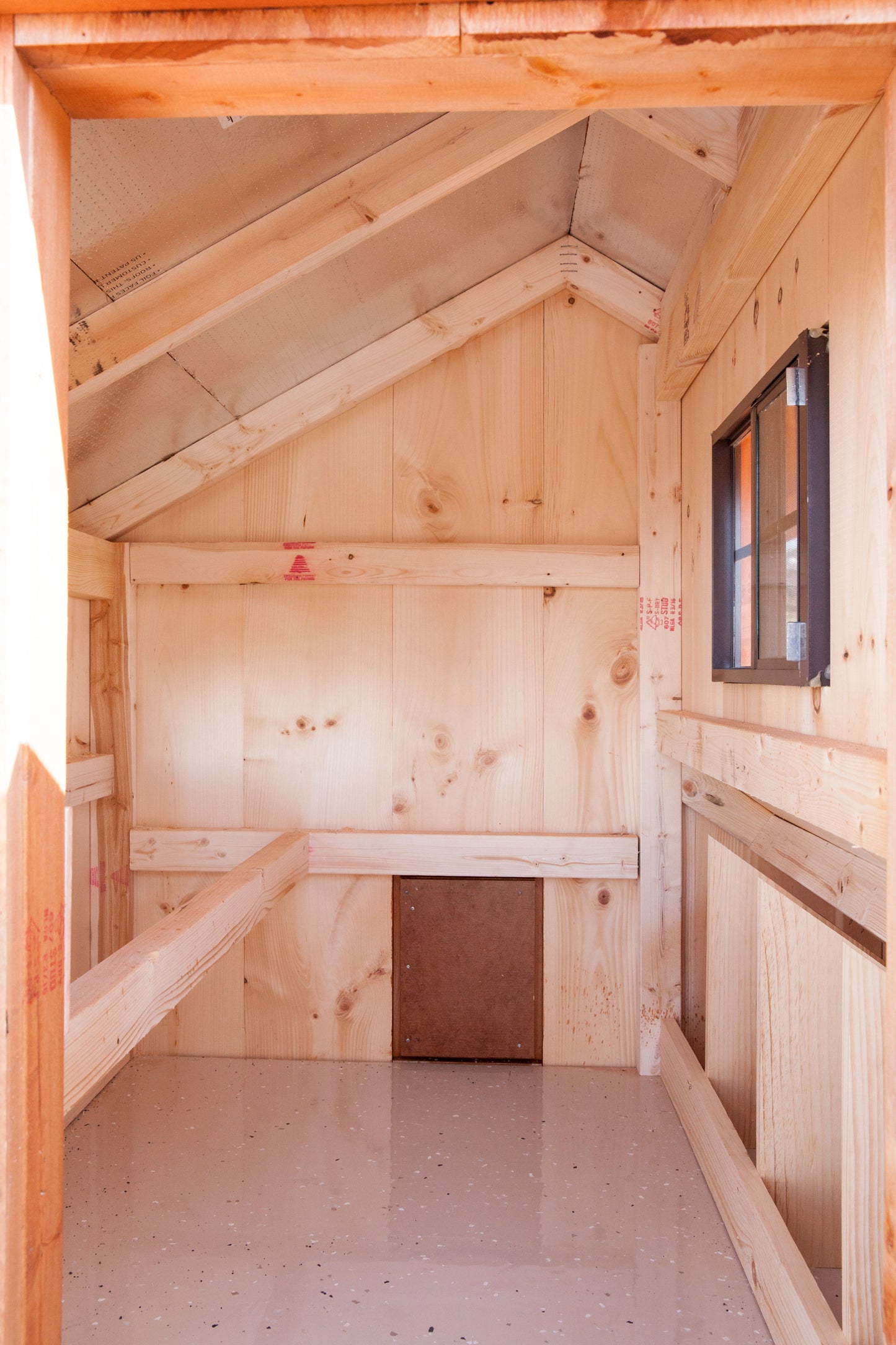Interior view of the 3x4 Amish-built Quaker chicken coop, showing a gray epoxy-coated floor, a small chicken access door on the left, and a window on the back wall.