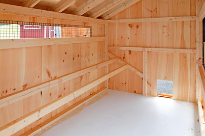 Interior view of an Amish-built wooden chicken coop featuring roost bars, natural wood walls, ventilation opening, and clean raised flooring