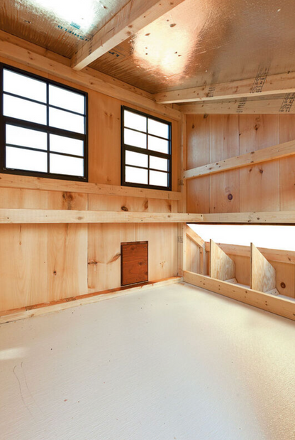 Interior of an Amish-built wooden chicken coop showing natural wood walls, insulated roof, windows for ventilation, and clean raised flooring