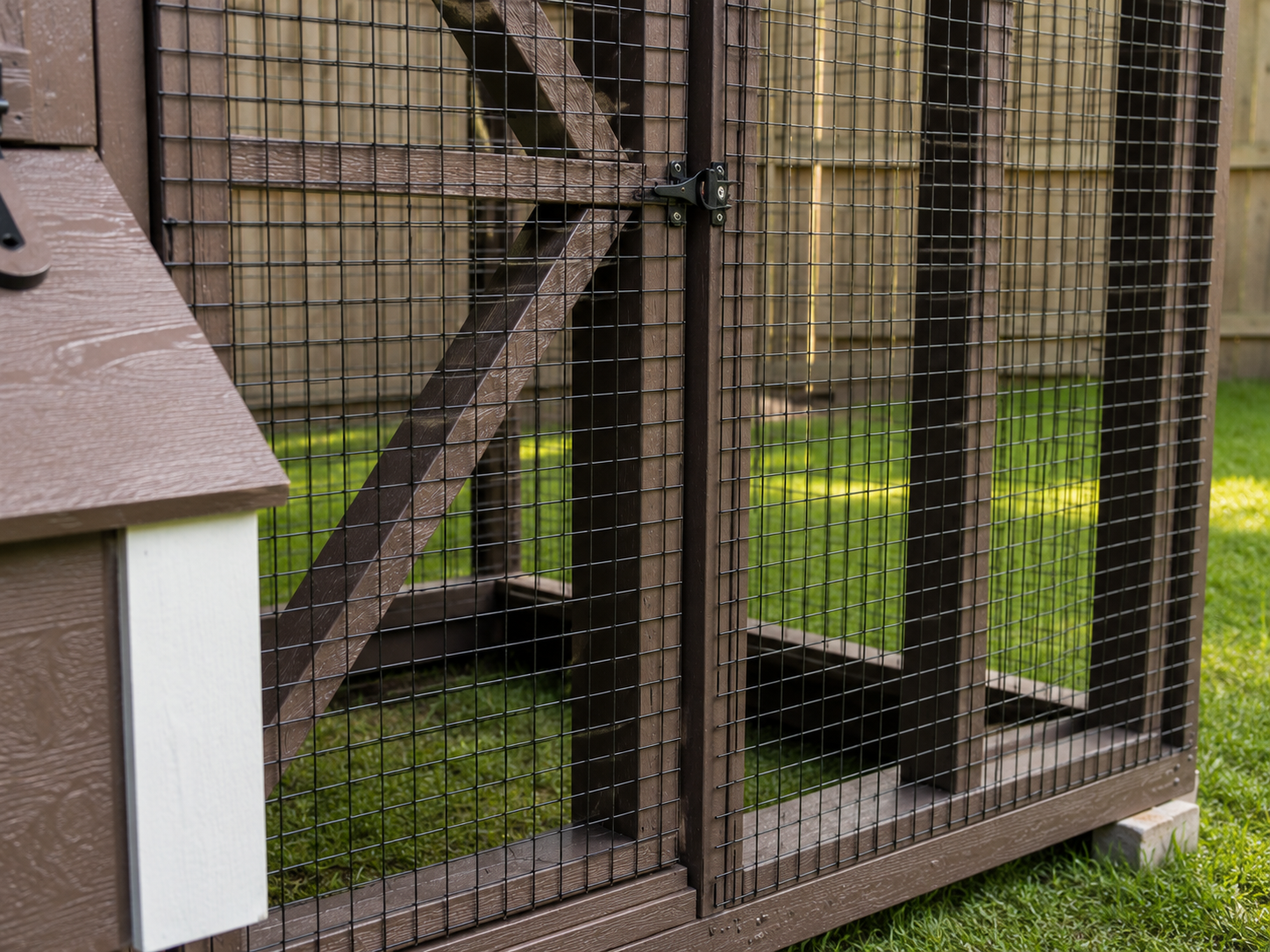 Close-up of black half-inch wire mesh on the chicken coop run with brown wood framing and backyard grass in the background.