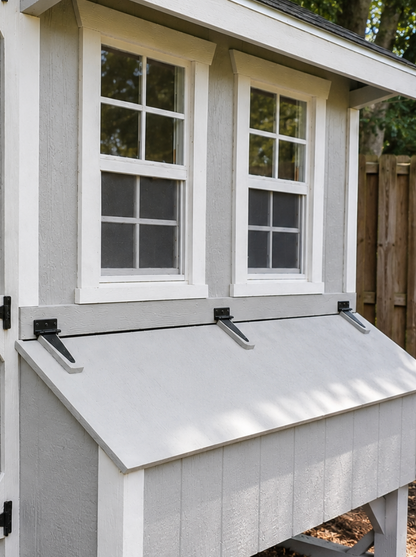 Close-up of a gray and white Quaker chicken coop showing wood texture, white trim, black hardware, windows, and front nesting box.