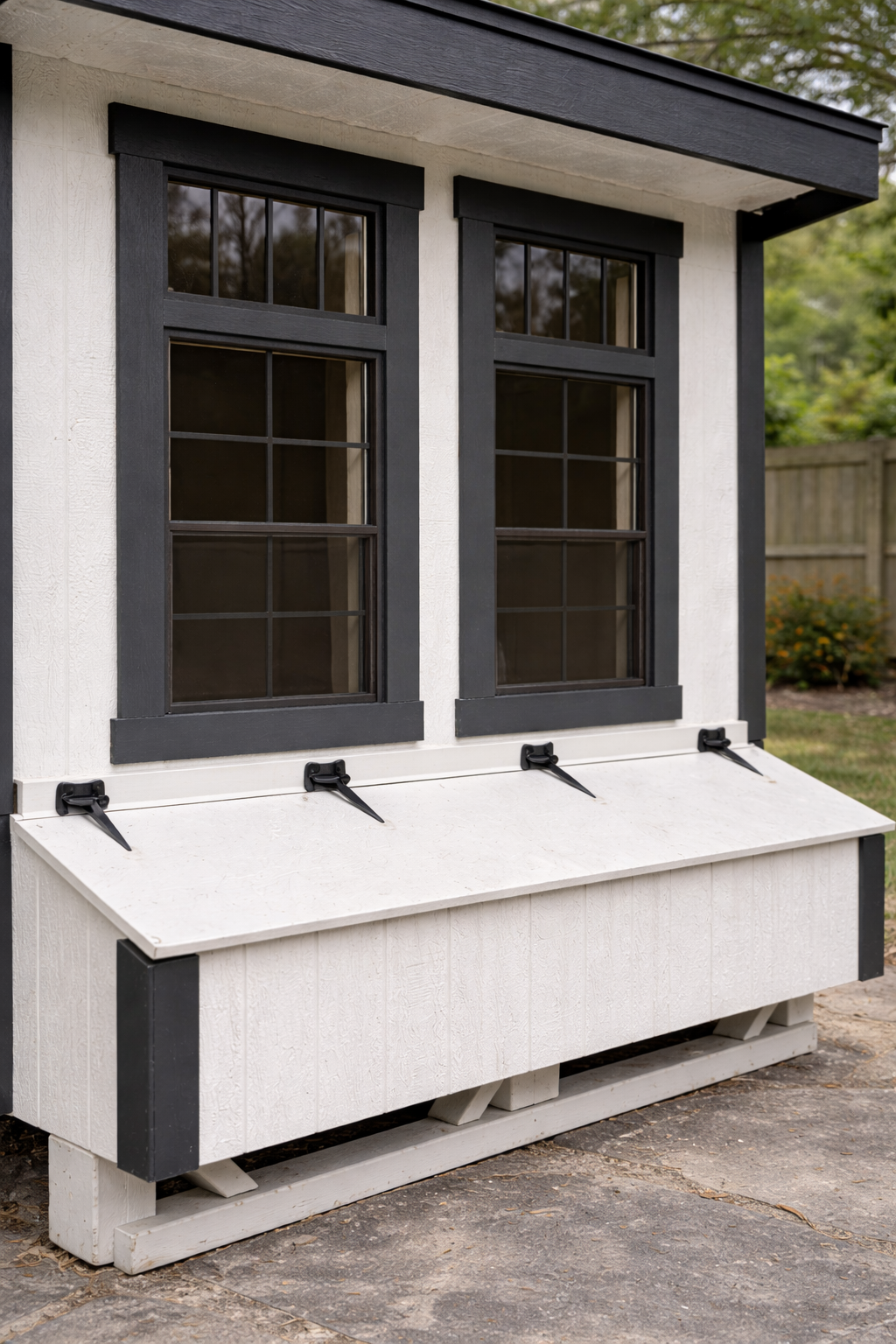 Close-up of Lean-To 7x8 Amish-built chicken coop showing board and batten siding, black trimmed double windows, and nesting box with metal latches in backyard setting.
